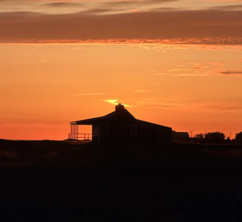 Nantucket cottage silhouetted against an orange sunset sky