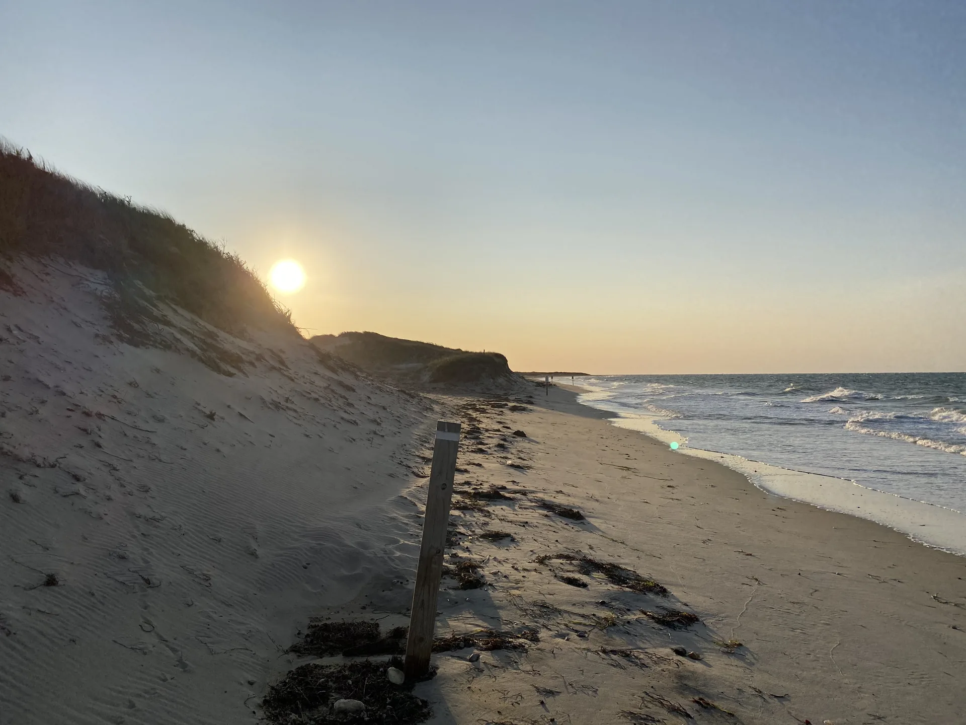 Late-September sunset at Eel Point, Nantucket: the sun dropping behind a grassy dune as small waves roll onto the empty beach