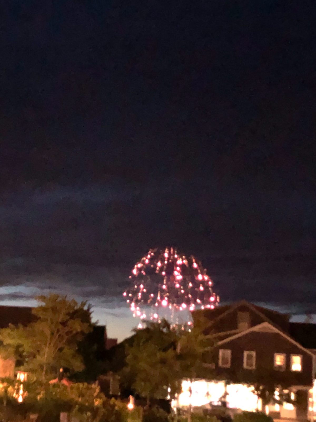 Red fireworks over the trees and shingled homes of Nantucket town
