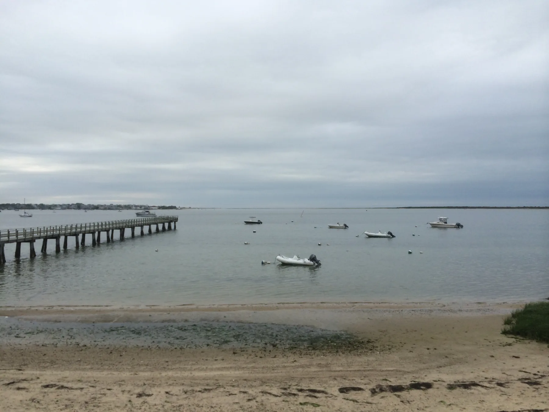 Weathered dock reaching into Nantucket Harbor with moored boats off Monomoy