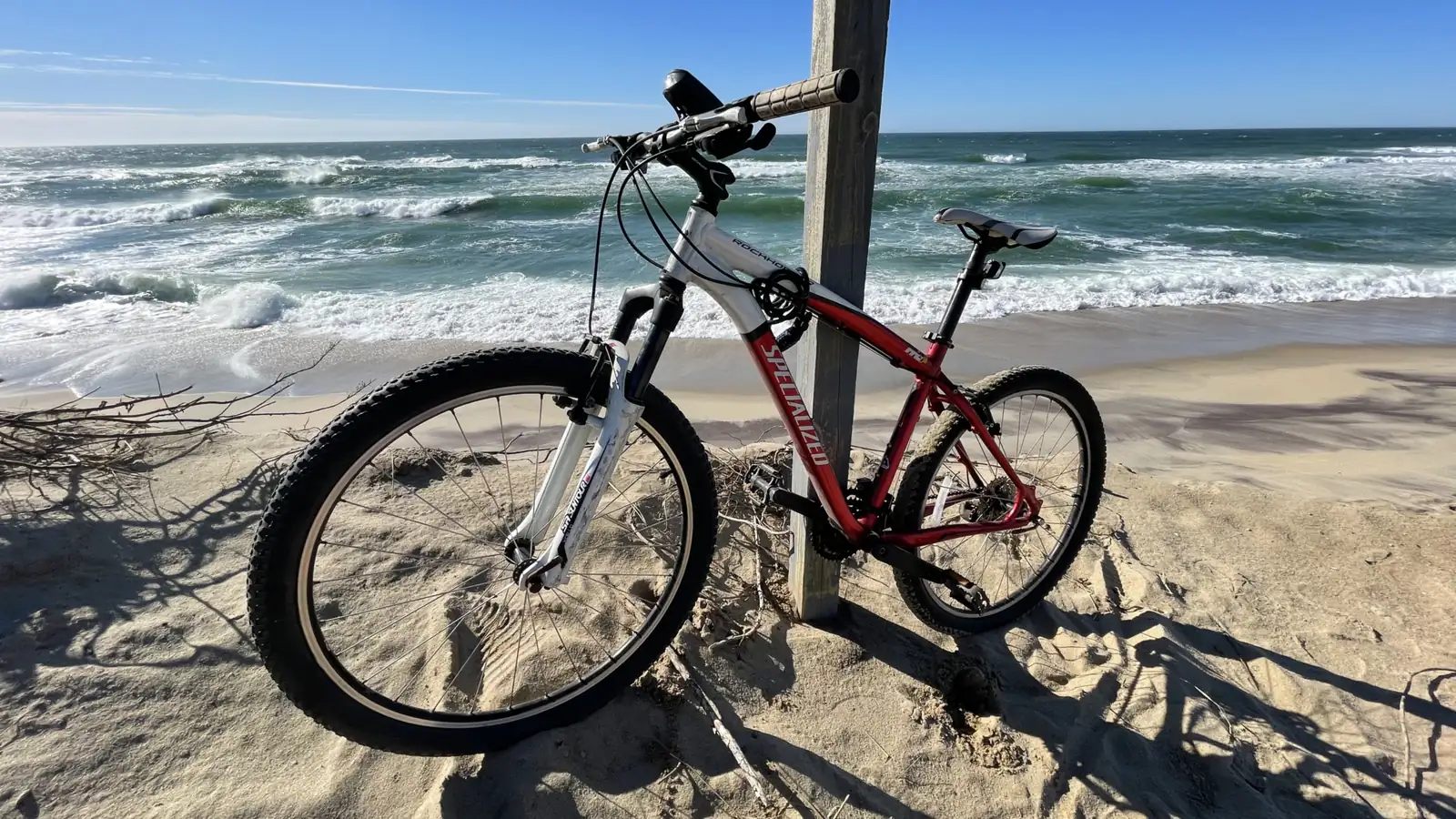A red mountain bike leaning against a weathered post at the top of a Nantucket beach, surf breaking beyond