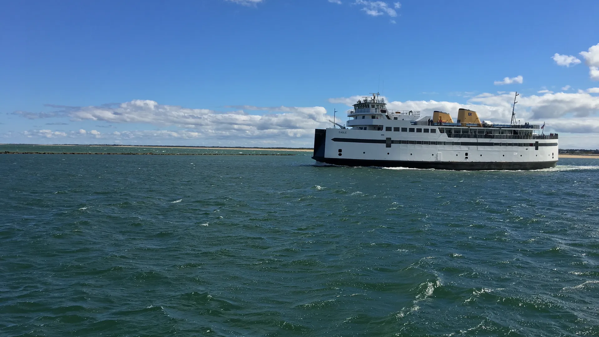 A Steamship Authority car ferry crossing choppy green water toward Nantucket under a bright, windy sky