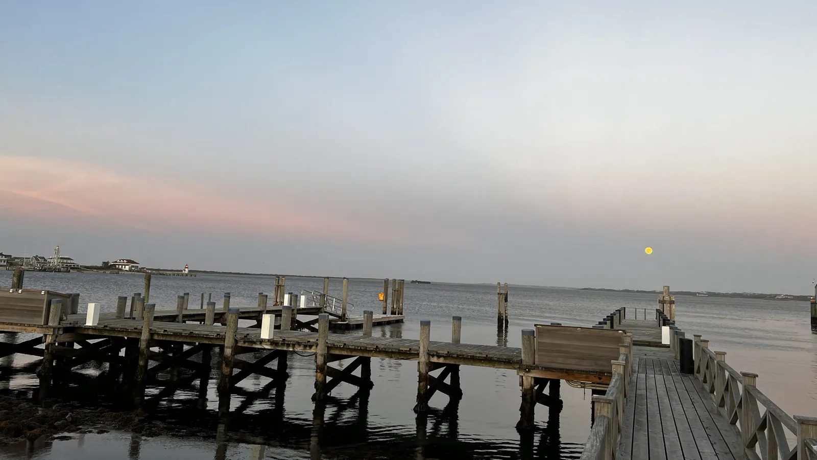 An empty dock on Nantucket Harbor at dusk in late autumn, the moon rising over still water