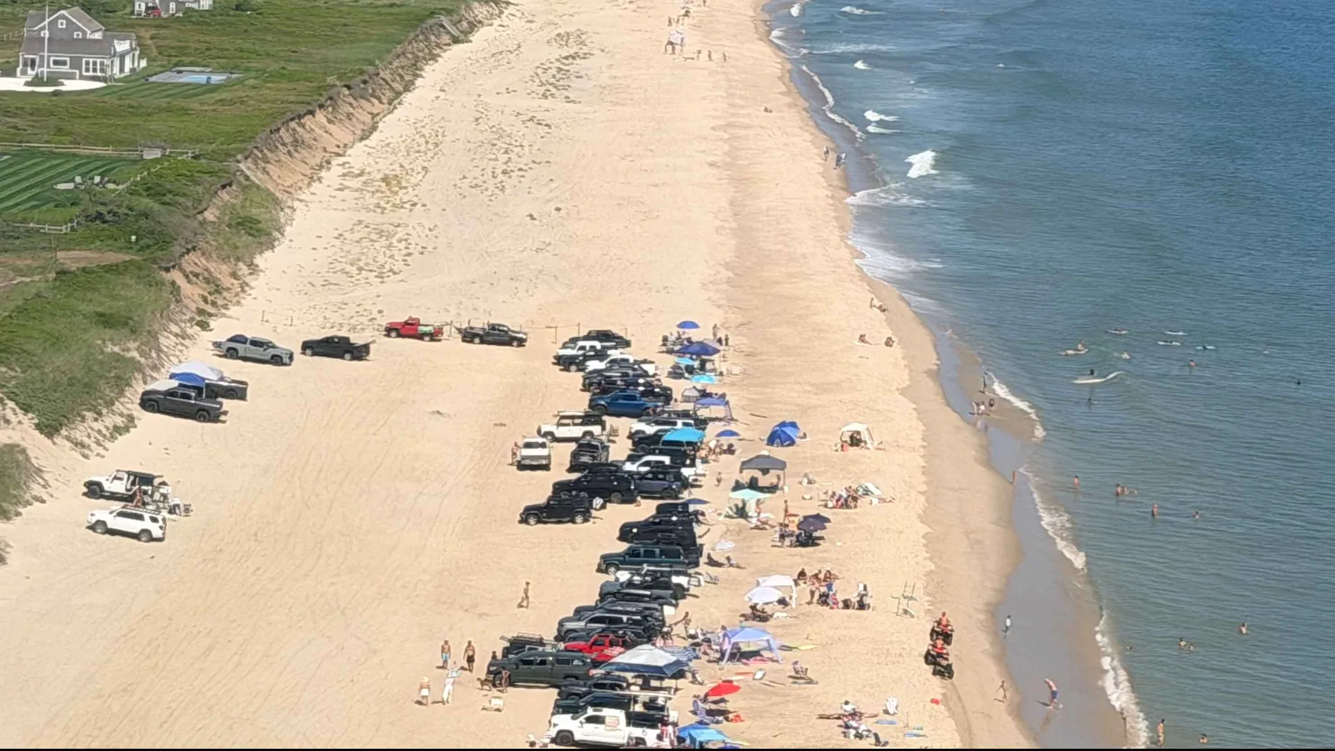 Summer aerial over Nobadeer Beach, just west of Madequecham: four-wheel-drive trucks and umbrellas lining the wide south-shore sand, swimmers in the break