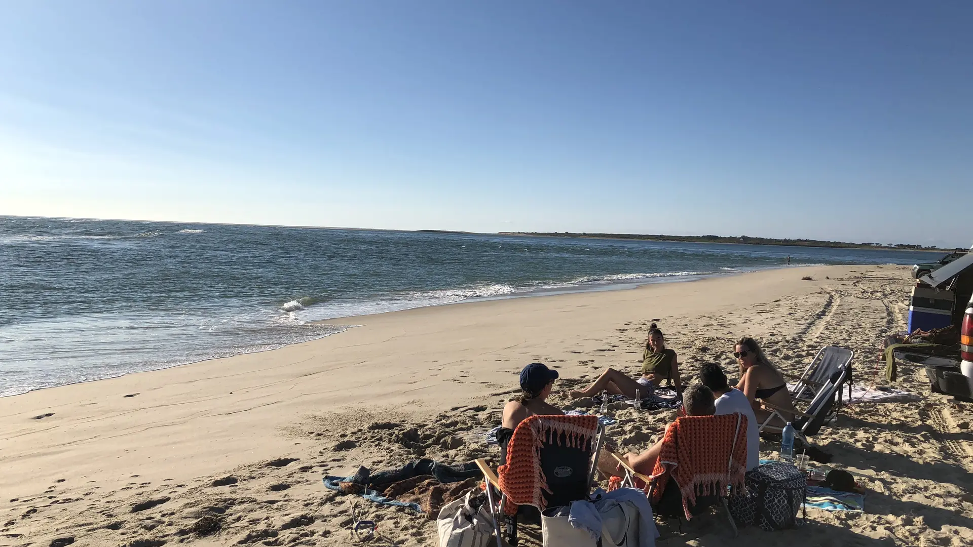 Late-day September sun on a wide, nearly empty south-shore beach on Nantucket, a few people settled in low chairs near the water