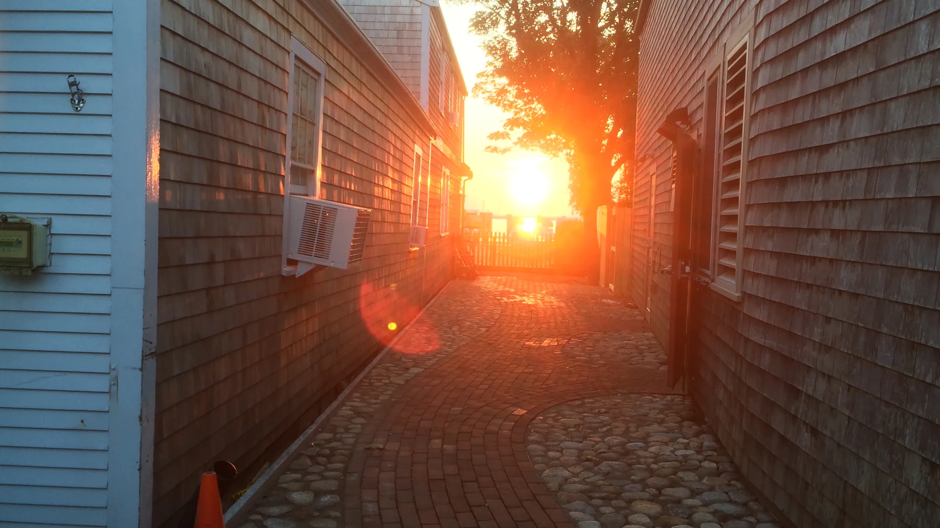 Low sun blazing down a narrow brick alley between two gray-shingled Nantucket houses