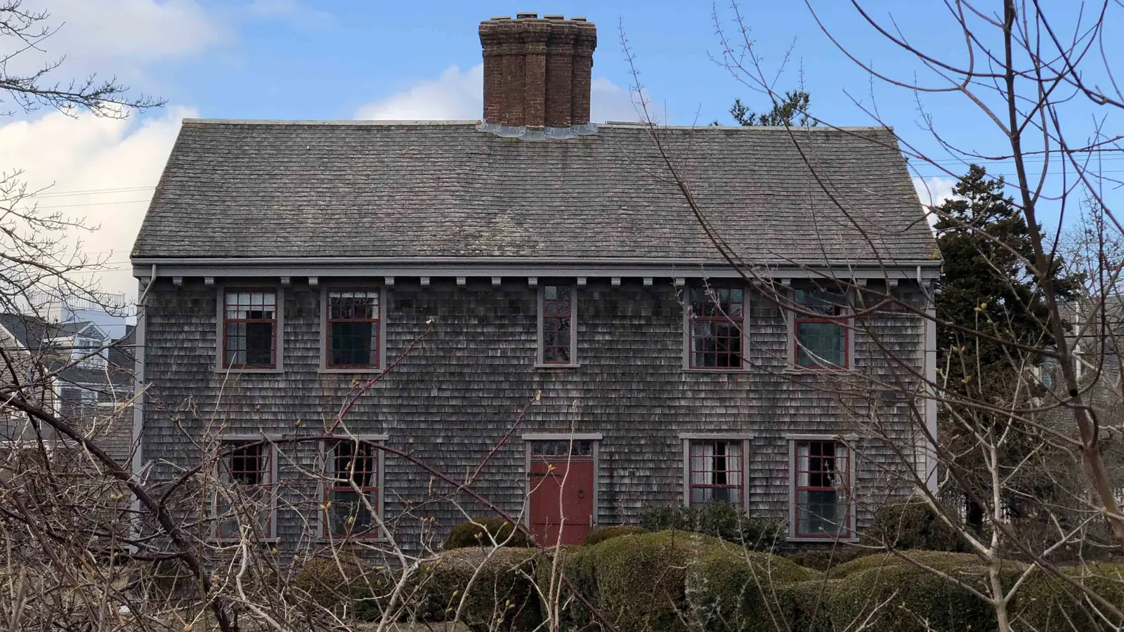 The Jethro Coffin House of 1686, Nantucket's oldest surviving house, its weathered grey shingles and central brick chimney seen through bare branches