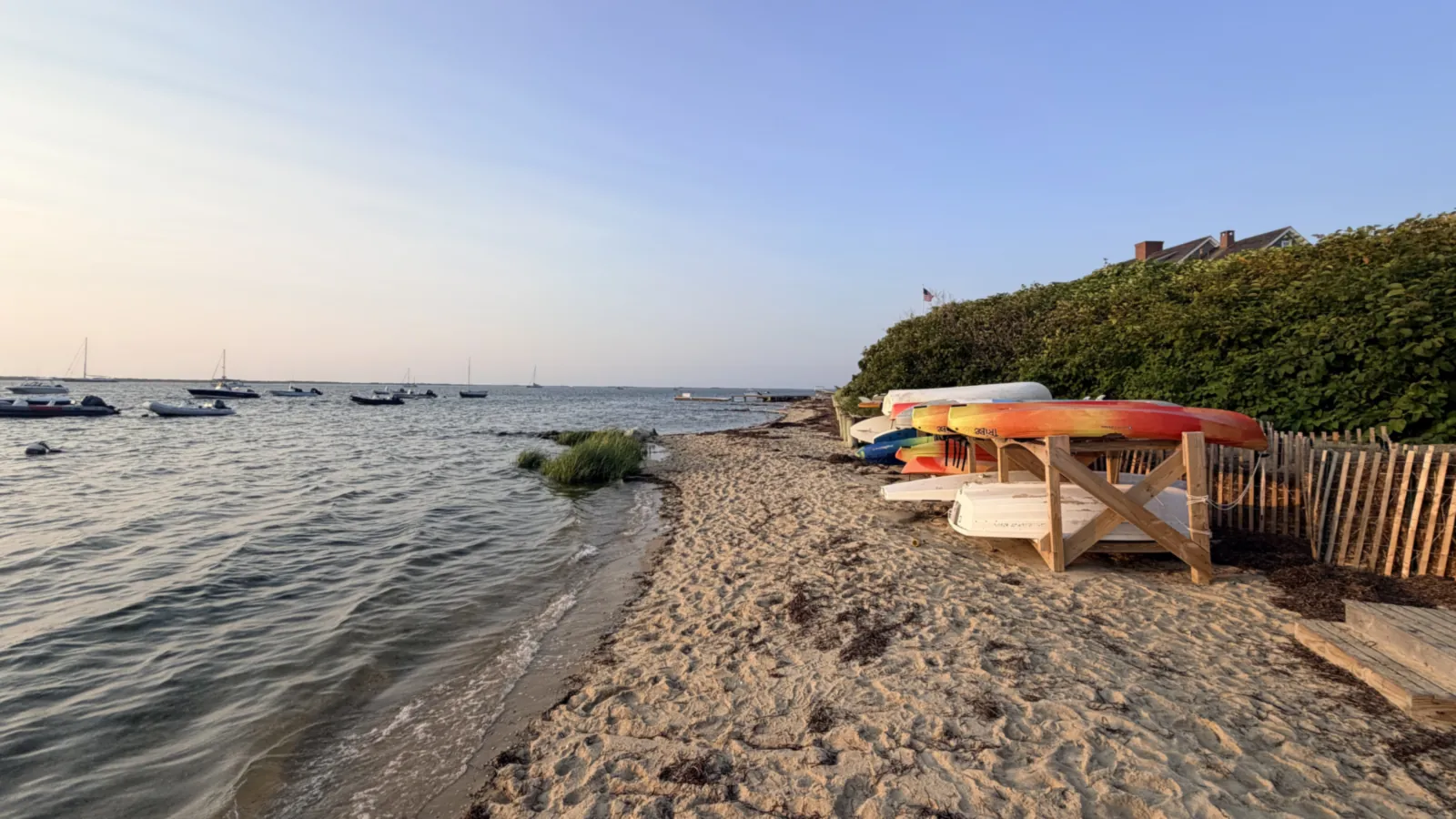 Shimmo's harbor beach in evening light, kayaks racked above the waterline and skiffs moored in the shallows