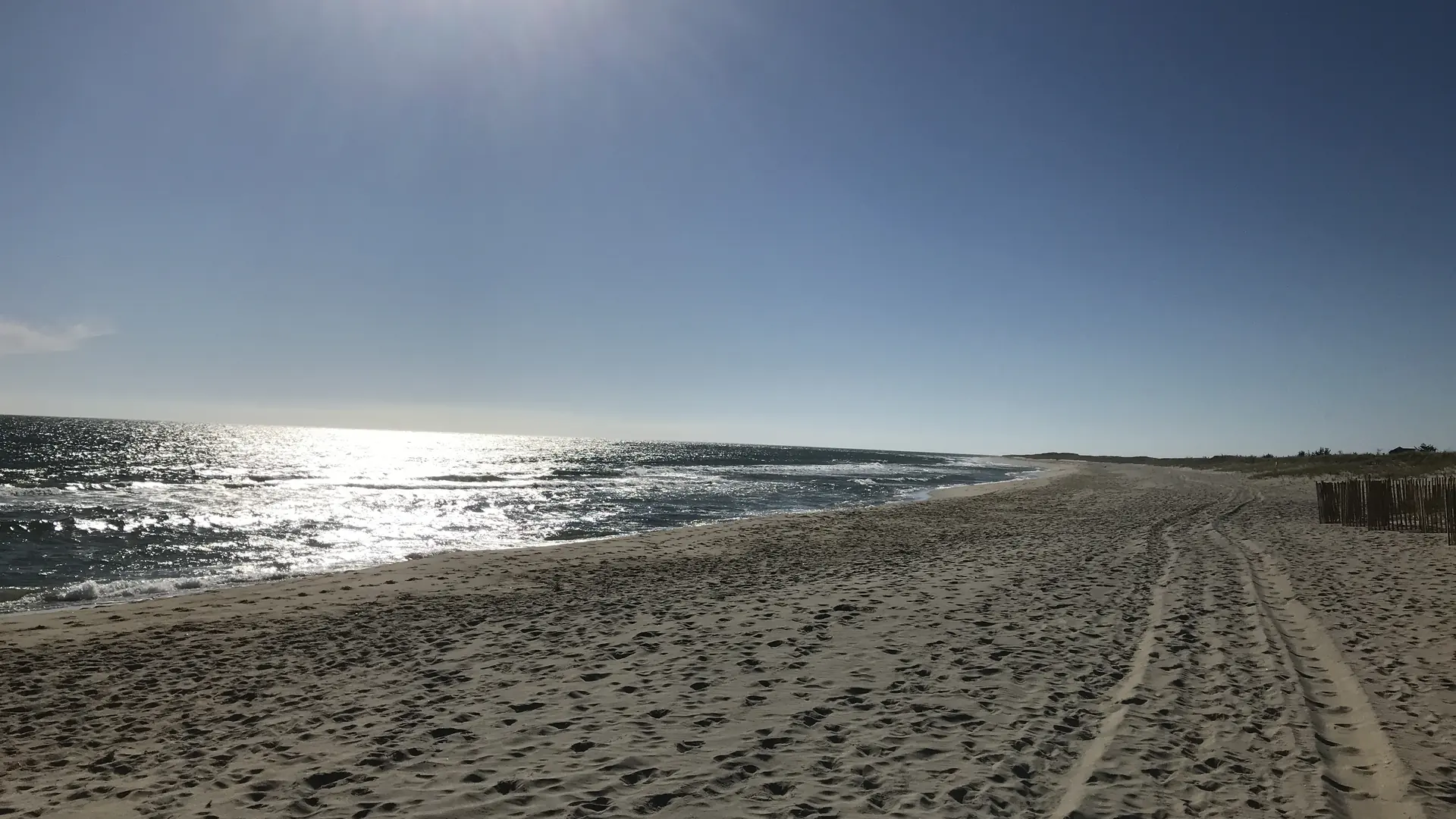 Tire tracks across an empty stretch of Surfside beach on an October afternoon, sun glinting off the water
